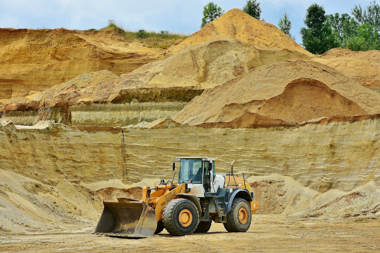 An excavator working in an open pit mine surrounded by sandy terrain and clear sky.